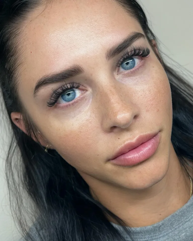 Portrait of a blue-eyed client wearing a wispy volume eyelash extension set with soft length and curled outer corners by Made by Marissa.