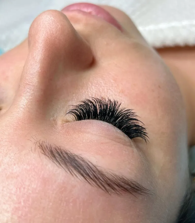 Angled close-up of a closed eye with a textured volume eyelash extension set and layered black fans by Made by Marissa.