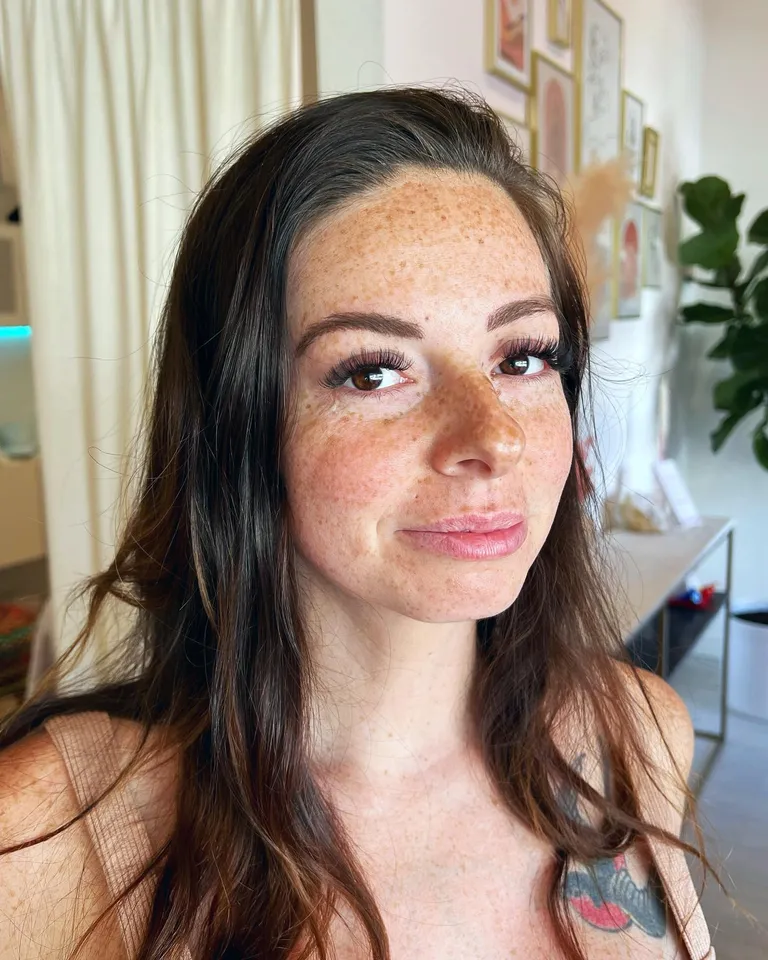 Portrait of a freckled client wearing a wispy volume eyelash extension set with a soft cat-eye silhouette by Made by Marissa.