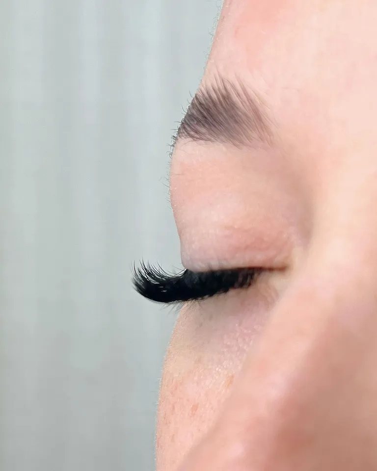 Side profile of a closed eye showing thick, curled volume eyelash extensions and a smooth dark lash line by Made by Marissa.