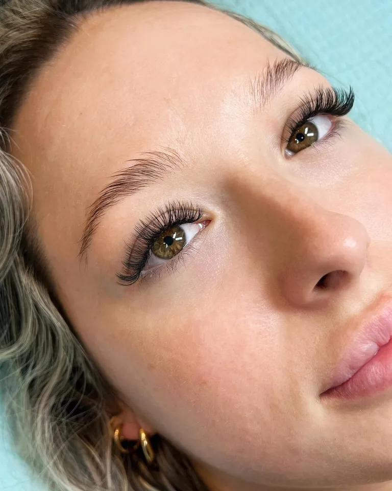 Portrait of a brown-eyed client wearing a balanced wispy volume eyelash extension set with softly tapered outer corners by Made by Marissa.