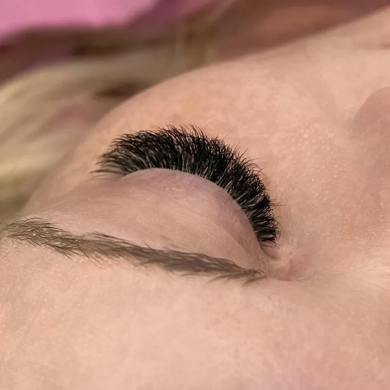 Side profile of a closed eye showing a dense, uniform volume eyelash extension set with a rounded curl by Made by Marissa.